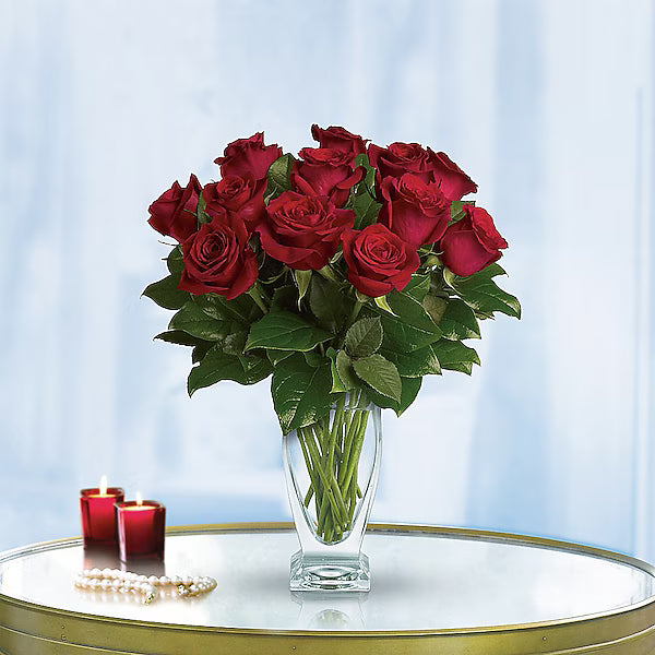 Elegant red rose bouquet in a transparent vase on a shiny table.