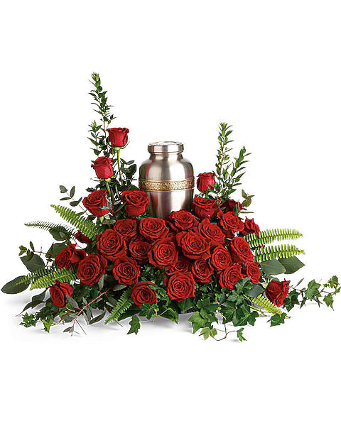Silver urn surrounded by lush red roses and fresh greenery on white backdrop