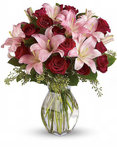 Bouquet of pink lilies and red roses in a clear vase on a white background