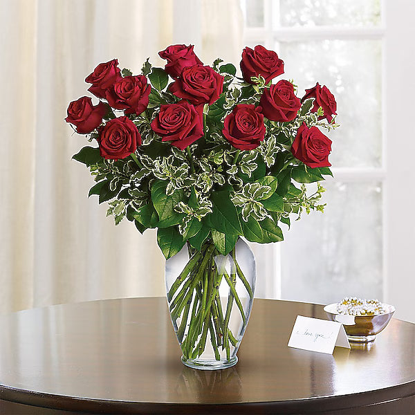 Glass vase of red roses on shiny surface before white drapery