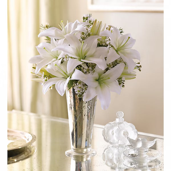 Bouquet of white lilies in a silver vase on a table with decorative items.