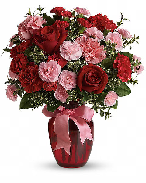 Red and pink floral bouquet in a red vase with a pink ribbon, sitting on a clean white tabletop