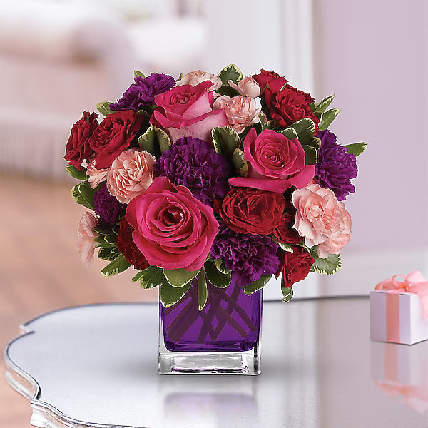 Mixed red, pink, and purple flowers in vase on reflective table